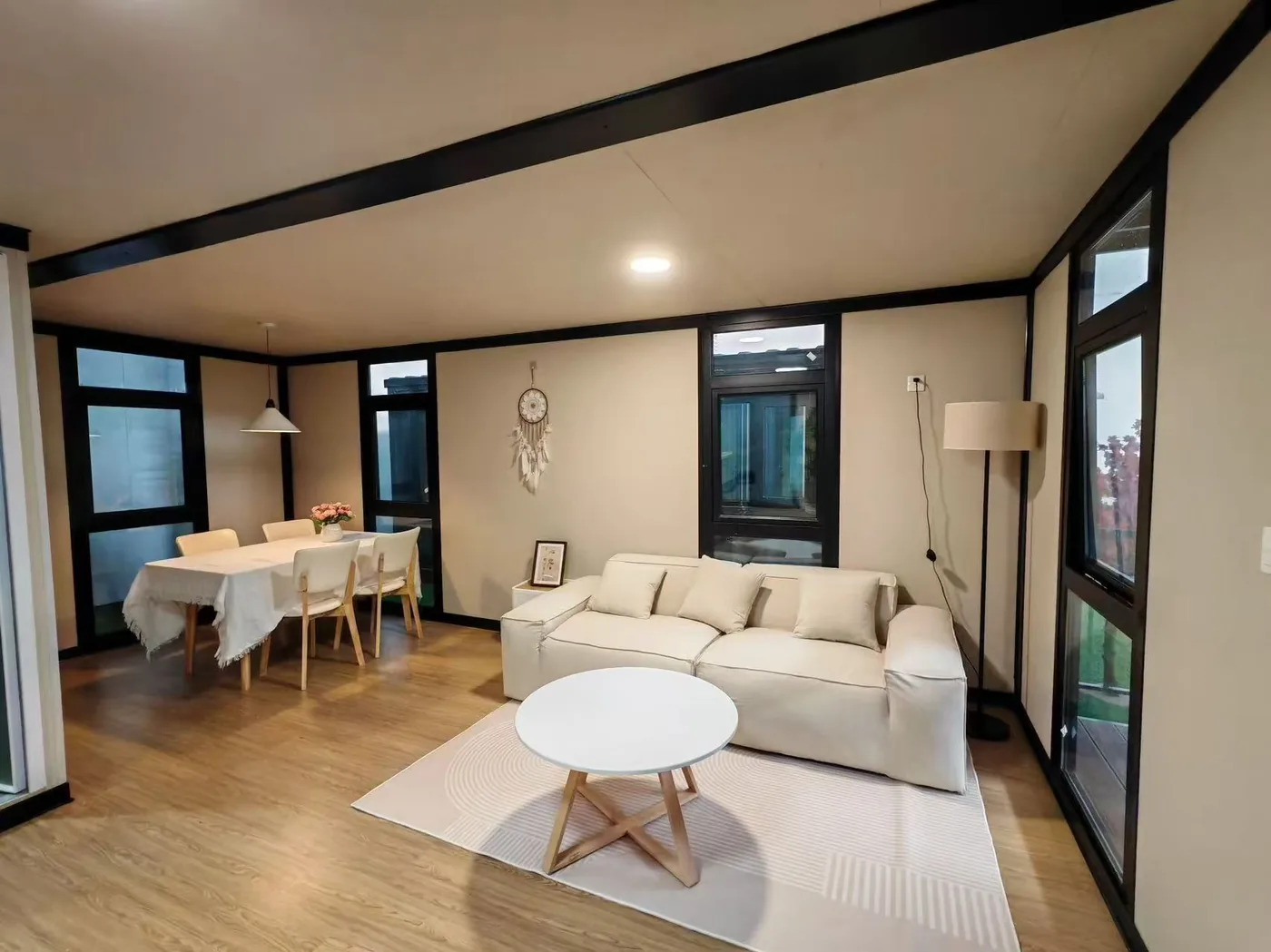 Obývací prostor rozkládacího domu Flexi House s pohovkou, jídelním stolem a okny do dvou stran